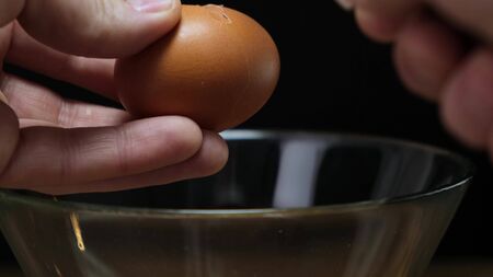 Hands holding one brown organic egg. Cracking over glass bowl.の写真素材