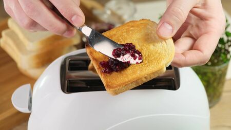 Tasty and hearty breakfast jam on crisp bread. Man makes a sandwich.