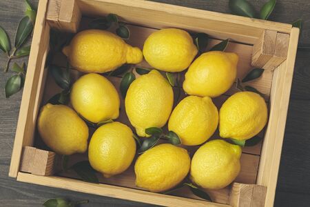 Wooden box of fresh lemons with tree leaves. Top view.の写真素材