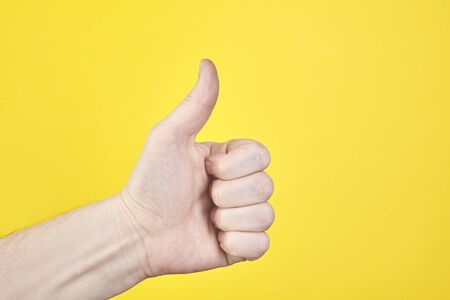 Male hand show one or like isolated on yellow background. Close up