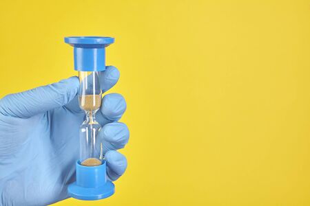 Dentist holding sand glass on yellow background. Copy space