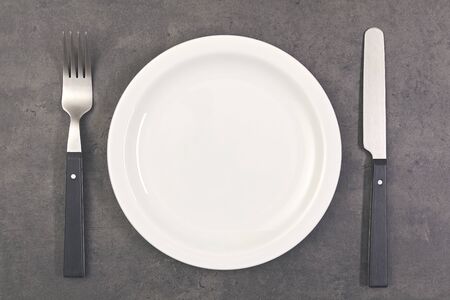 top view of white plate with knife, spoon on gray concrete surfaceの写真素材