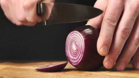 Hands cut red onions in kitchen on wooden board. Close up.