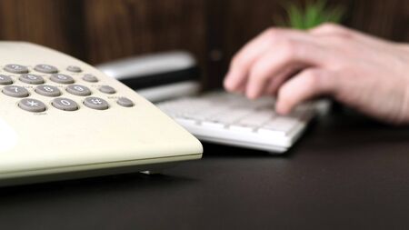 Hands of a man is using a computer, typing on keyboard, call the phone.