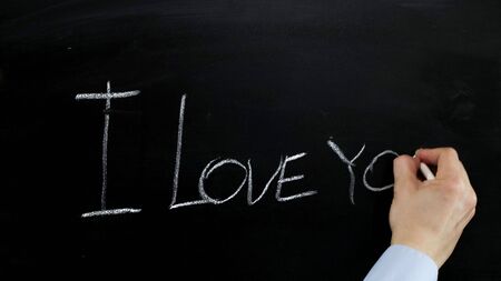 Hand writes with chalk I love you on blackboard. Close up.