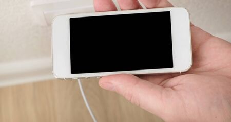 white smartphone on charge. Connecting cable to the phone. Close up.