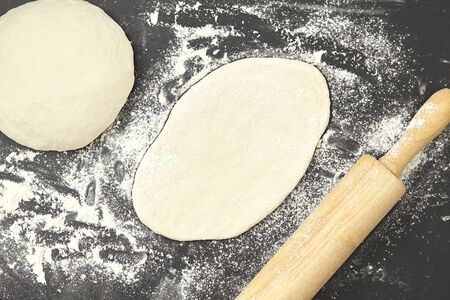 Dough and wood rolling pin on clean black background top view
