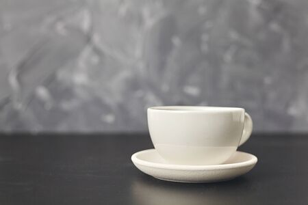 A white cup on the black table. On gray background