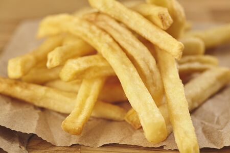 French fries in a paper on wooden table. Close up