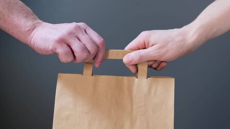 Close up hold in hand brown clear empty blank craft paper bag for give takeawayの写真素材