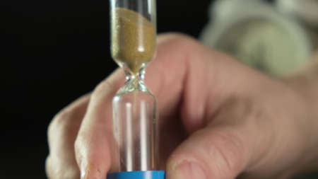 Mans hand flips an hourglass. Close up on black