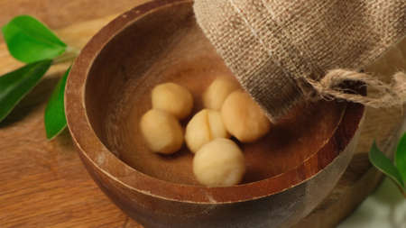 Macadamia nuts fall into wooden wood bowl on board. Close up.の写真素材