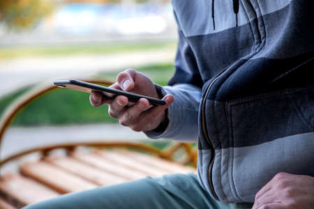 Profile of a guy using a smart phone sitting on a bench in a parkの写真素材