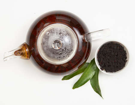 Teapot and cup of tea with green leaves on whiteの写真素材