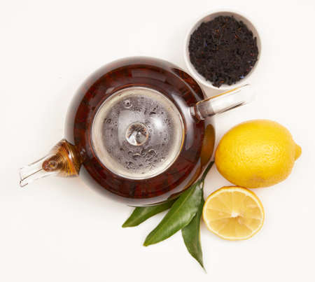 Teapot and cup of tea with green leaves and lemon on whiteの写真素材