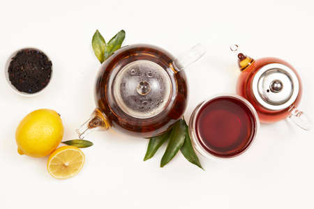 Teapot and cup of tea with green leaves and lemon on whiteの写真素材