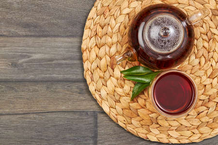 A glass kettle and a cup of hot black tea on a wooden table.の写真素材