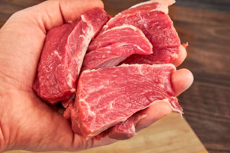 fresh raw steak in human hand isolated on wooden backgroundの写真素材