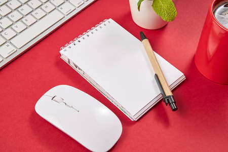 Red office desk table with blank notebook, keyboard and coffee cup. Top view with copy space.の写真素材