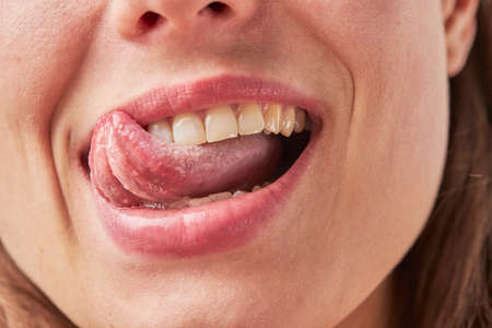 Beautiful young woman leaking teeth with tongue close-upの写真素材