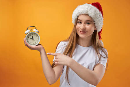 Woman in Santa Claus hat with alarm clock on background isolated. Close up