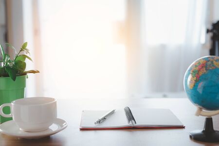 cup of coffee on the table, Wood office desk table With a notepad, pen and coffee, Behind the window...