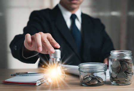business man holding a light bulb with taking notes and a jar with coins inside, Concept idea energy...