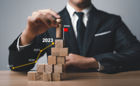 Starting the new year 2023, businessman plans to set goals in life successful in 2023, strategic develop concepts change mindset to become the top leader, holding a wooden doll on a cube that Stacked.の写真素材