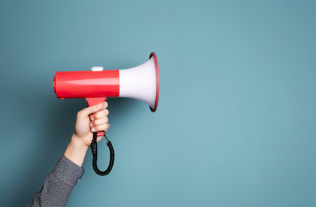 Hand holding a megaphone on a blue background with copy spaceの素材