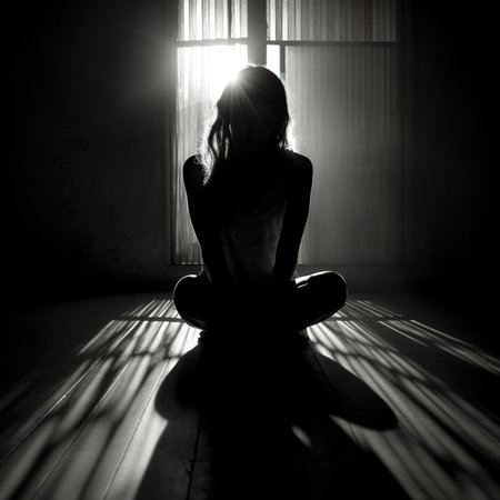 Silhouette of a young woman sitting on the floor in the dark.の素材