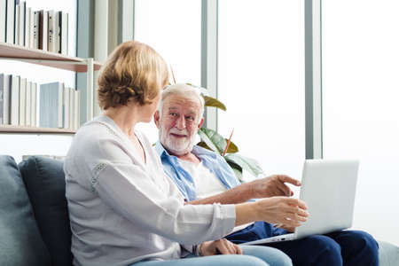 Elderly senior family couple sitting in modern living room together using laptop with smile happy and romantic emotion.の写真素材