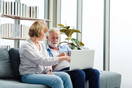 Elderly senior family couple sitting in modern living room together using laptop. Old man get confuse from modern technology.の写真素材