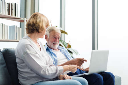 Elderly senior family couple sitting in modern living room together using laptop. Old man get confuse from modern technology.の写真素材