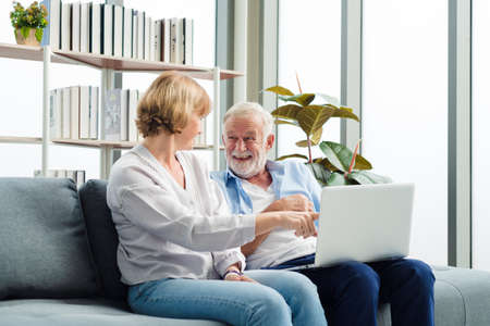 Elderly senior family couple sitting in modern living room together using laptop with smile happy and romantic emotion.の写真素材