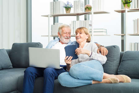 Elderly senior family couple sitting in modern living room together using laptop with smile happy and romantic emotion.の写真素材