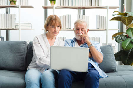 Elderly senior family couple sitting in modern living room together using laptop. Old man get confuse from modern technology.の写真素材