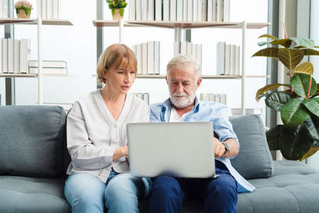 Elderly senior family couple sitting in modern living room together using laptop. Old man get confuse from modern technology.の写真素材