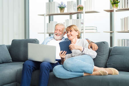 Elderly senior family couple sitting in modern living room together using laptop with smile happy and romantic emotion.の写真素材