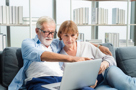 Elderly senior family couple sitting in modern living room together and using laptop.の写真素材