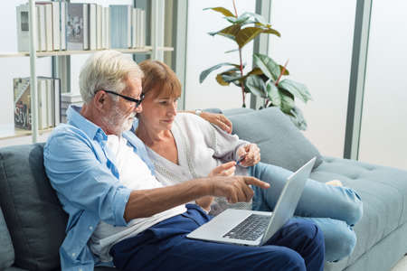 Elderly senior family couple sitting in modern living room together and using laptop to shop online with credit card.の写真素材