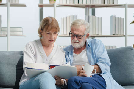 Elderly senior family couple in casual outfit embracing and using smart tablet with smile happy and romantic emotion in living room.の写真素材