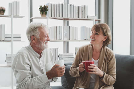 Portrait of senior elderly couple in casual outfit sitting on couch and drink a cup of coffee...