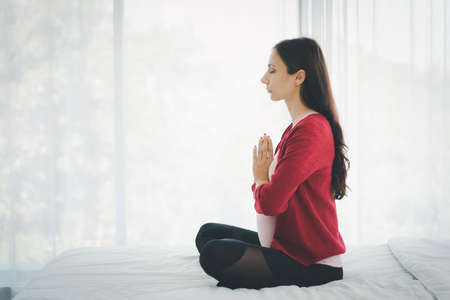 Portrait of pregnant woman in casual home outfit sitting on bed and practice yoga in modern bedroom.の写真素材