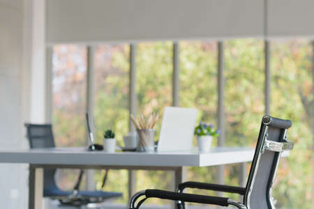 Modern design office room with couple of chairs and 1 table and pencil, notebook, small vase, pen, and coffee cup on table, Nature outside window backgroundの写真素材