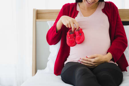 Pregnant woman in casual outfit plan and prepare his or her children outfit for their future in modern bedroom.の写真素材