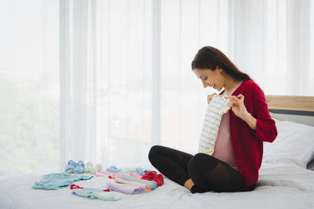 Pregnant woman in casual outfit plan and prepare his or her children outfit for their future in modern bedroom.の写真素材