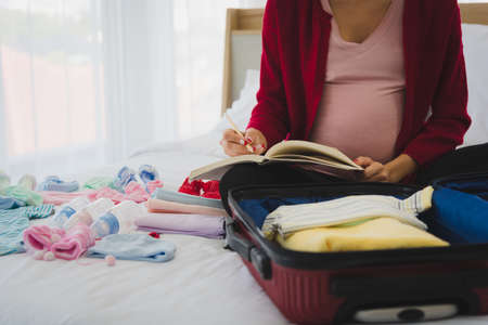 Pregnant woman in casual outfit writing and planning accessories for her children for their future in modern bedroom.の写真素材