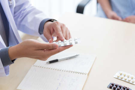 Asian doctor in professional work uniform discuss and explain about pills and medicines symptoms to his patient.の写真素材