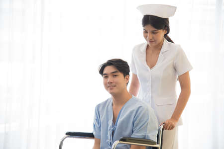 Asian nurse in working uniform taking care of patient sitting on wheel chair.の写真素材