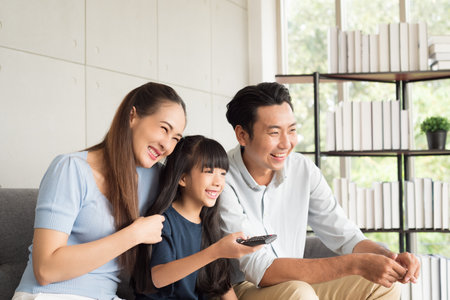 Happy mother father and daughter family sitting on couch and watching television together relaxing at home.の写真素材